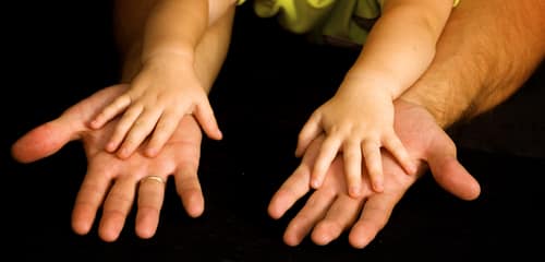 man's hands over child's hands