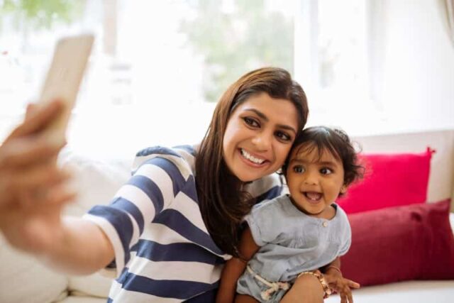Smiling Indian young woman taking selfie with her little daughter