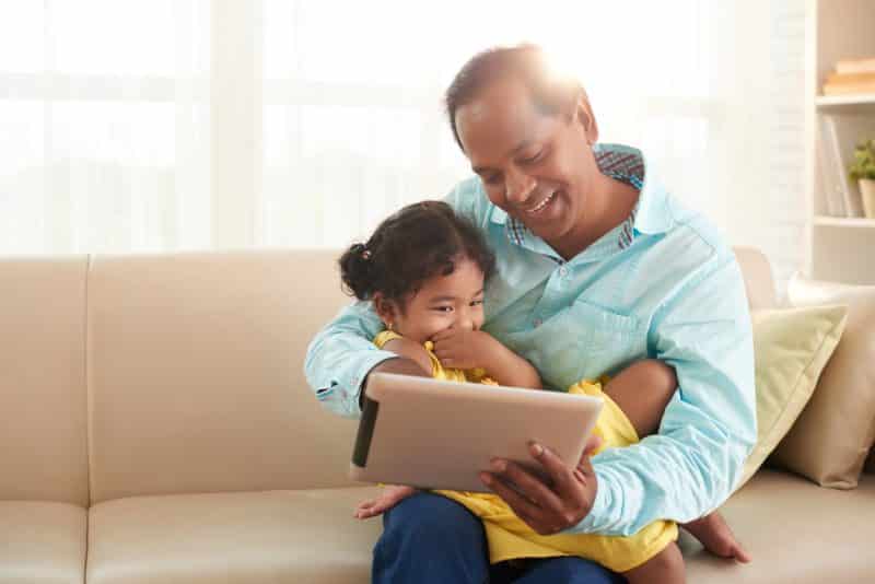 Cheerful Indian man and his daughter watching cartoons on digital tablet