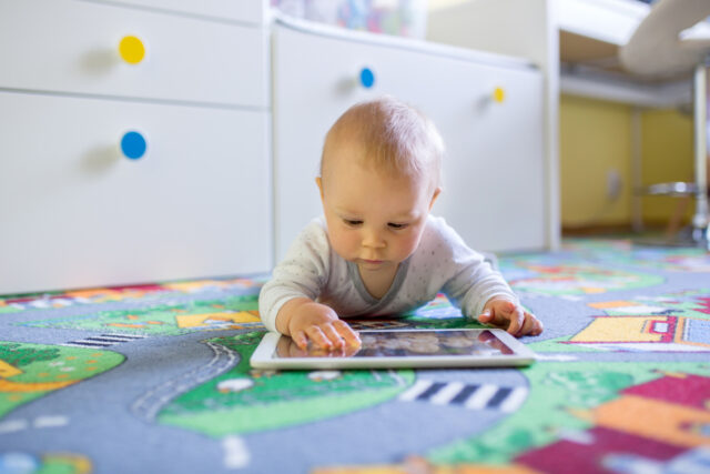 Portrait of cute little toddler child, playing on tablet, baby boy smiling happily